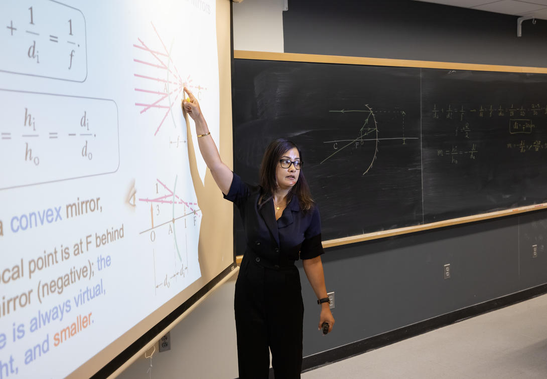 Female physics professor points to equation on white board. 
