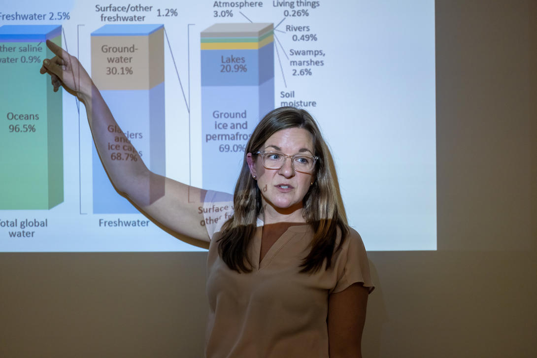 Female chemistry professor stands in front of a smart board pointing to data sets.