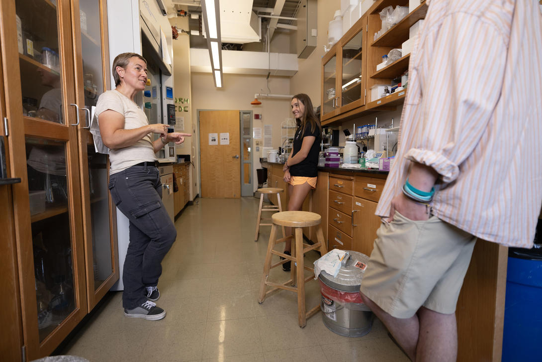 Female biology professor talks with two students in her lab.