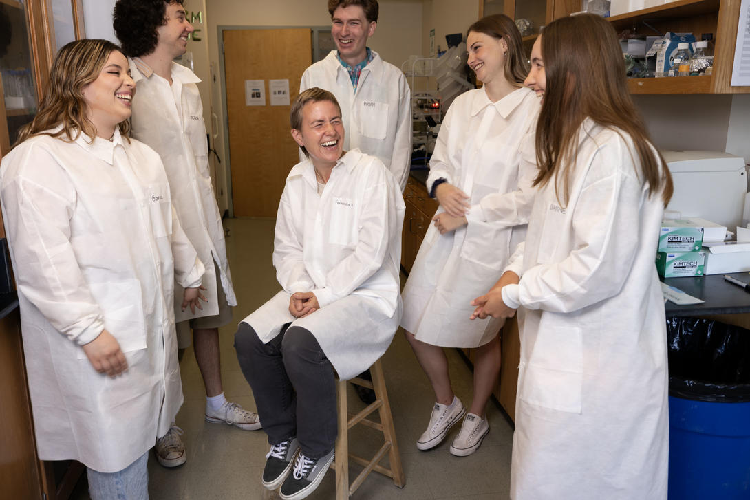 Female biology professors laughs with students in her lab.