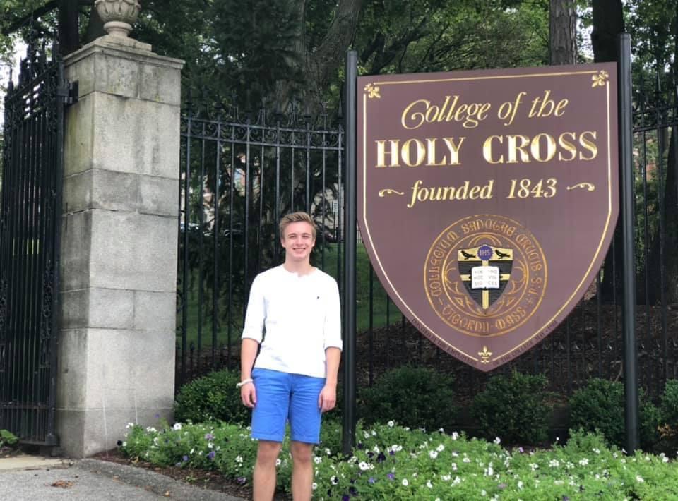 A young Kevin Hamilton standing next to a Holy Cross sign